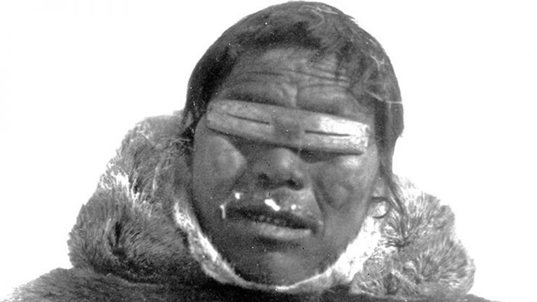 Inuit man wearing snow goggles he made out of bone