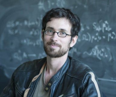 Portrait of a man sitting in front of a blackboard filled with equations